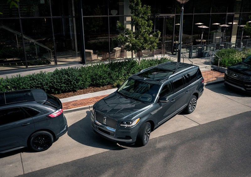 A 2023 Lincoln Navigator® SUV is being parallel parked between two vehicles on a downtown street outside of a luxury hotel. | Gary Yeomans Lincoln Ocala in Ocala FL