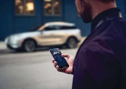 A person is shown interacting with a smartphone to connect to a Lincoln vehicle across the street. | Gary Yeomans Lincoln Ocala in Ocala FL