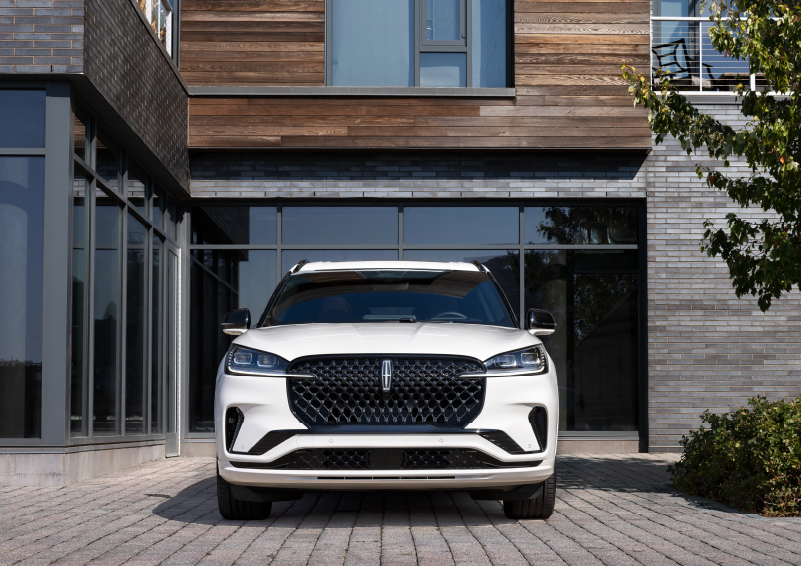 A white 2025 Lincoln Aviator® SUV is shown parked outside a modern building with gray brick and wood accents. | Gary Yeomans Lincoln Ocala in Ocala FL
