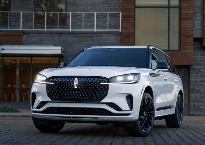 A white 2025 Lincoln Aviator® SUV is shown parked outside a modern building with gray brick and wood accents. | Gary Yeomans Lincoln Ocala in Ocala FL