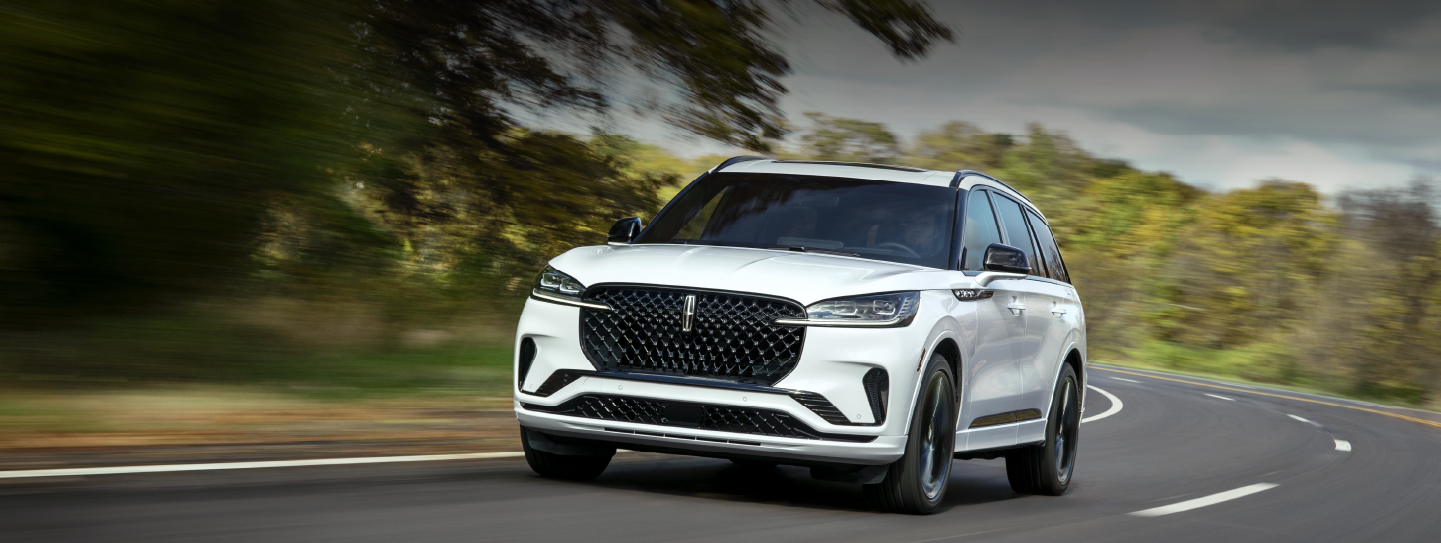 A white 2025 Lincoln Aviator® SUV is being driven down a road lined with trees. | Gary Yeomans Lincoln Ocala in Ocala FL