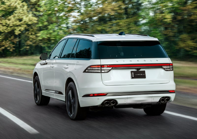 A white 2026 Lincoln Aviator® SUV is being driven away down a road lined with colorful trees. | Gary Yeomans Lincoln Ocala in Ocala FL
